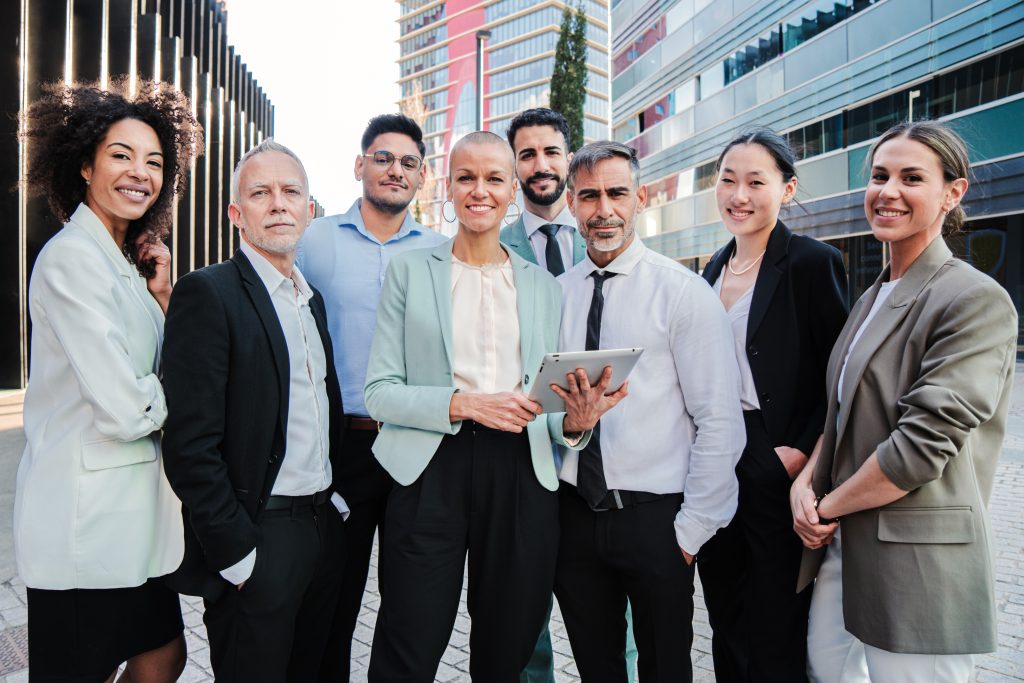 Team work of businesspeople standing at workspace and looking at camera together. Meeting of a crowd of corporate coworkers. Partnership of startup successful employees colaborating at job. Profession. High quality photo